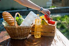 A Hand Holds A Tomato Over A Basket. Donation Box With Food. Fruits, Vegetables, Canned Food, Milk And Sunflower Oil In Stock Images