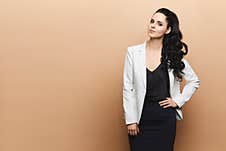 Elegant Young Woman With Dark Hair In The Skirt, Blouse And White Jacket Posing At The Beige Background, Studio Shot Royalty Free Stock Images