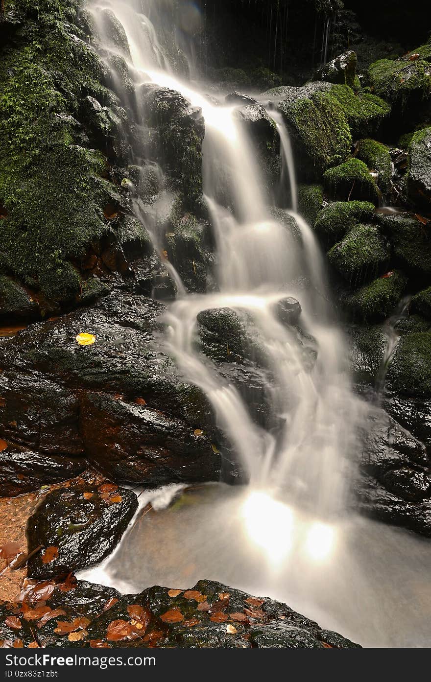 Nature - beautiful small waterfall on the creek. Natural colorful background with running water over stones in the forest