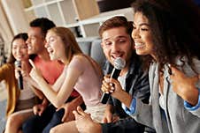 Friends And Music. Joyful Friends Looking Excited While Playing Karaoke At Home, Singing With Microphone, Sitting On The Royalty Free Stock Images