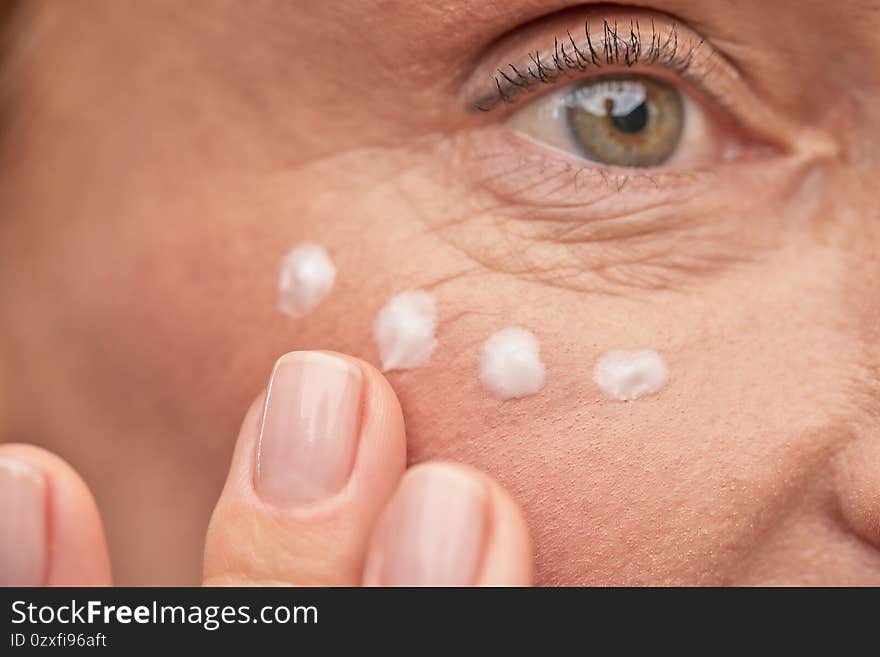 Close up of mature woman applying cosmetic product under eyes. Beauty treatment and wellness concept. Close up of mature woman applying cosmetic product under eyes. Beauty treatment and wellness concept