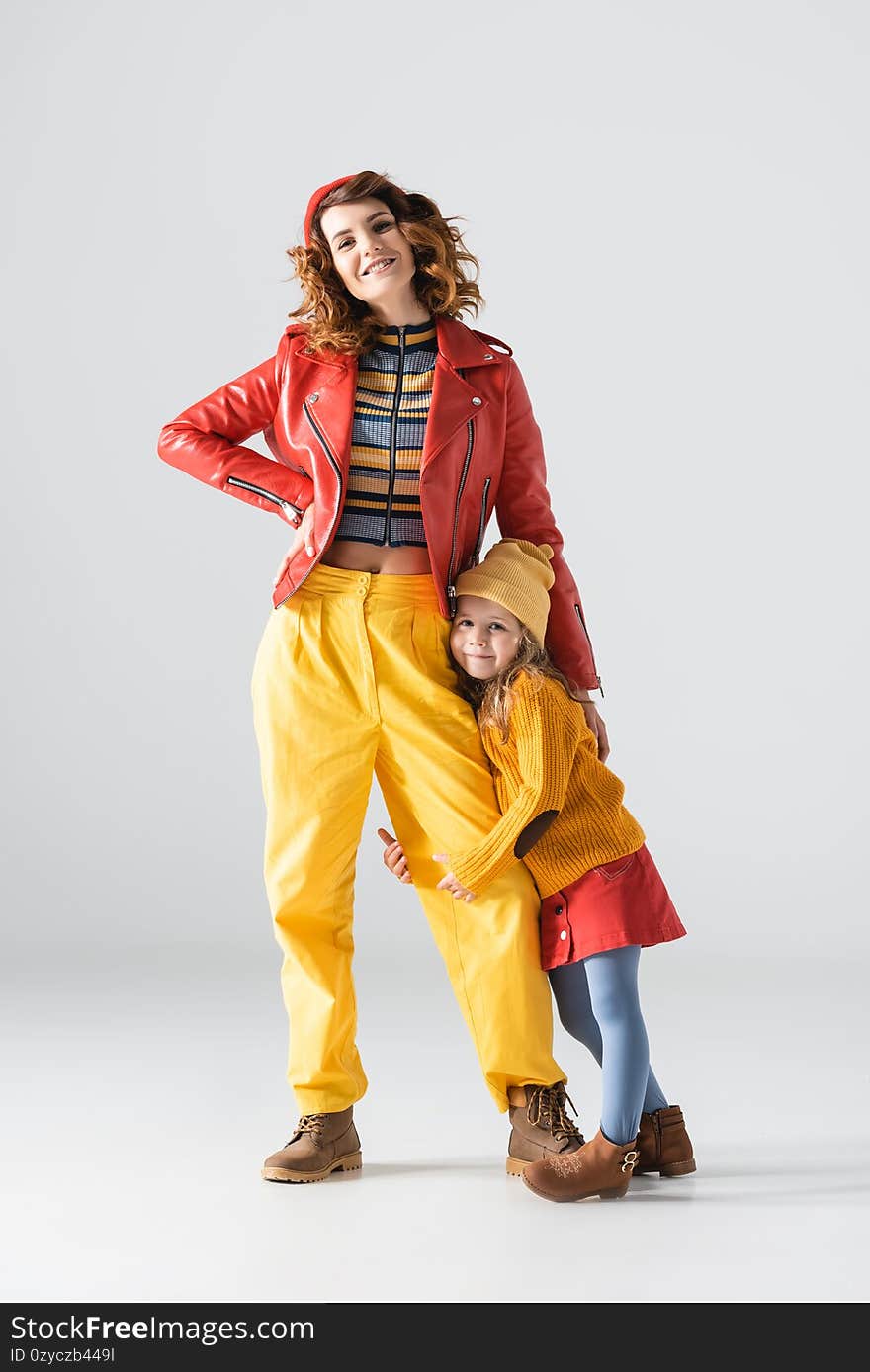 Daughter in colorful red and yellow outfit hugging mother leg on grey background