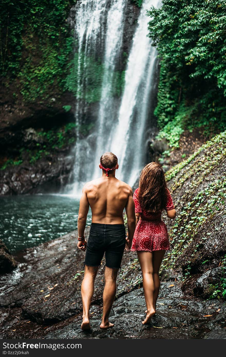 Tourists at the waterfall, rear view. Couple on vacation in Bali. Honeymoon trip. A couple in love travels the world. Vacation on the island of Bali. Tourists in Bali. Copy space