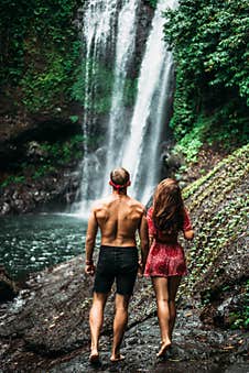 Tourists At The Waterfall, Rear View. Couple On Vacation In Bali. Honeymoon Trip. A Couple In Love Travels The World. Royalty Free Stock Photo