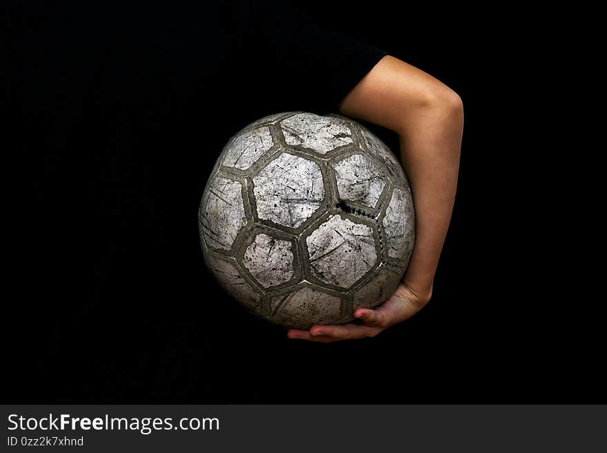 Old soccer ball in the hands of a teenager on a black background.