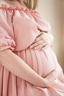 Pregnant Woman At Home In Pink Dress Hugs Her Belly Stock Photography