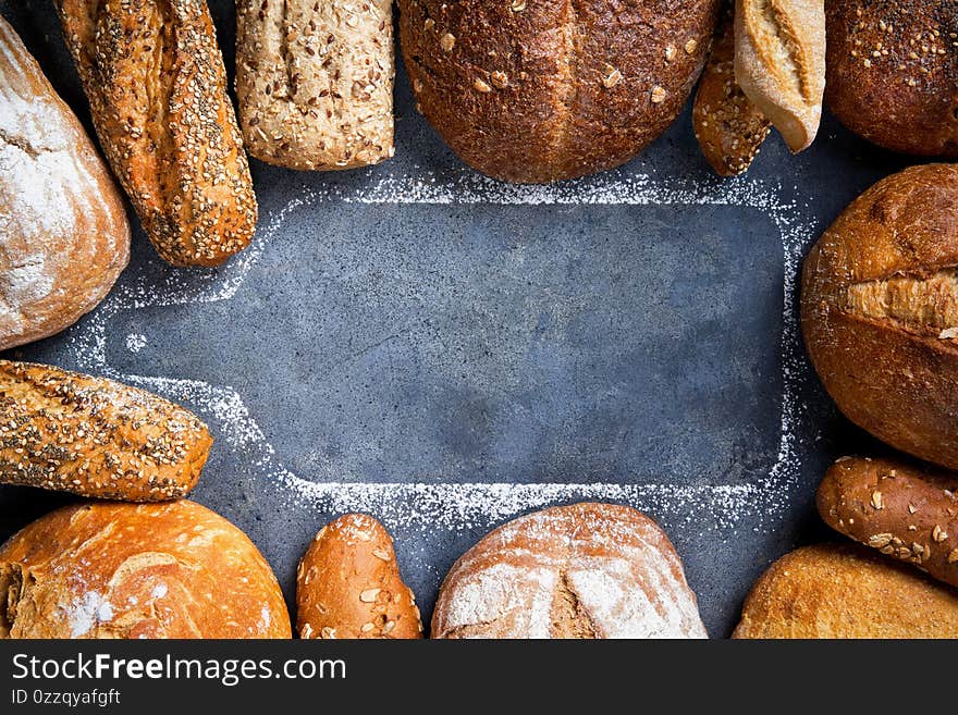 Banner with different types of fresh bread surrounded by a silhouette wooden cutting board on a gray surface, top view, copy space