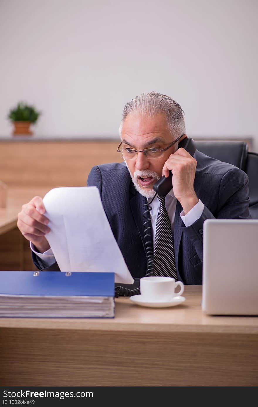 Old male employee reading paper in the office