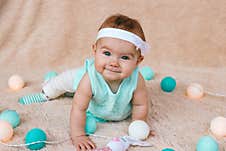 Cute Smiling Little Girl With Beautiful Blue Eyes In Blue Dress Is Sitting On A Beige Plush Plaid With Christmas Lights Before Stock Photography