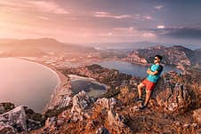 Confident Man In Sunglasses And Red Shorts Surveys The Surrounding Area From A Viewpoint. In The Background, A Colorful Sunset Stock Images