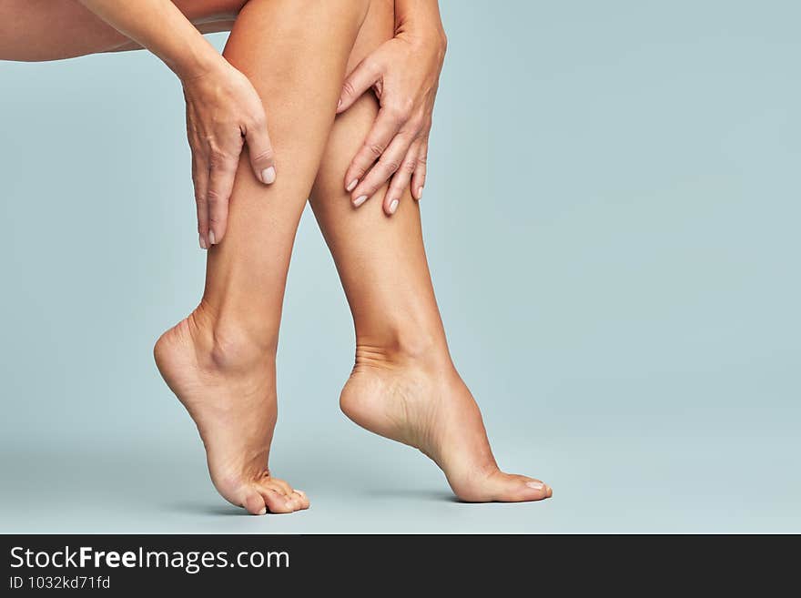 Cropped shot of a woman touching her legs with smooth, silky and soft skin after making a depilation, sitting over blue