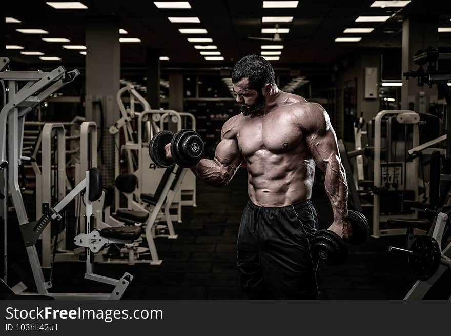 success concept of strong young male bearded athlete lifting heavy weight dumbbells in fitness sport gym