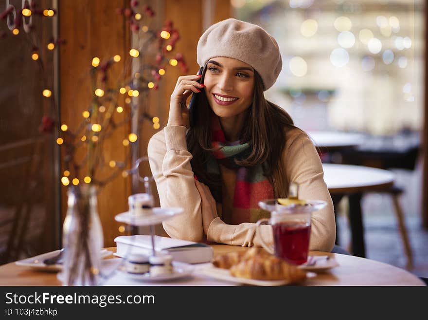 Happy young woman sitting at desk in the cafe and talking on her mobile phone