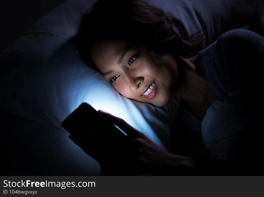 Young woman using a smartphone in her bed at night