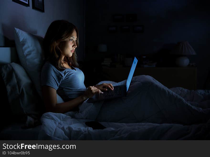 Young woman using a laptop in her bed at night