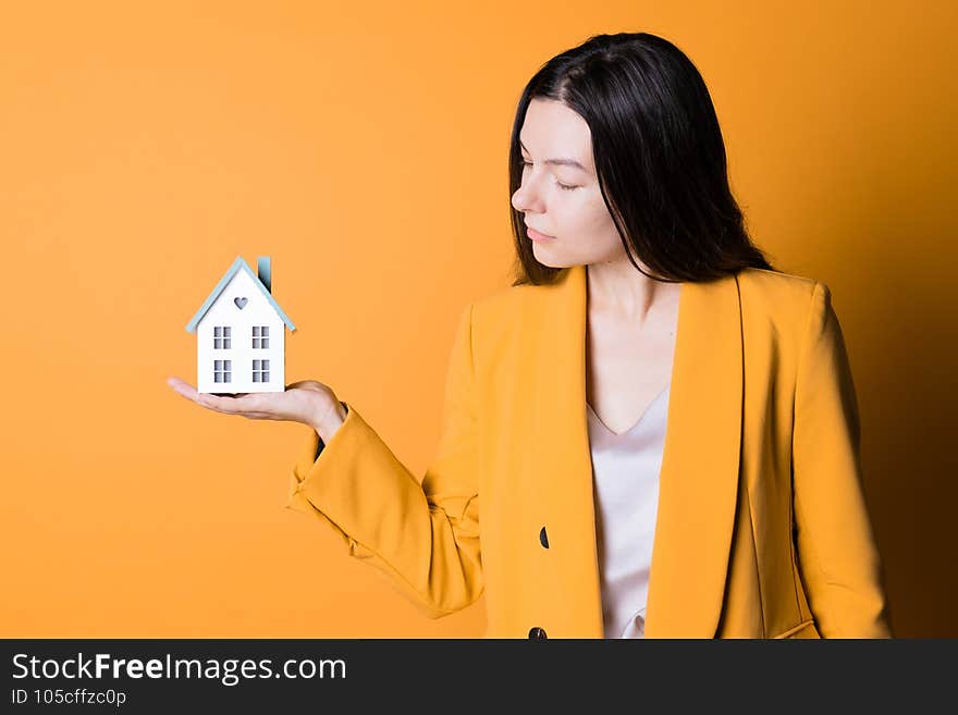 Take a mortgage, lending for the purchase of real estate. A young woman with a small house in her hands on a bright yellow background. Financial goals for the family, the purchase of their home.