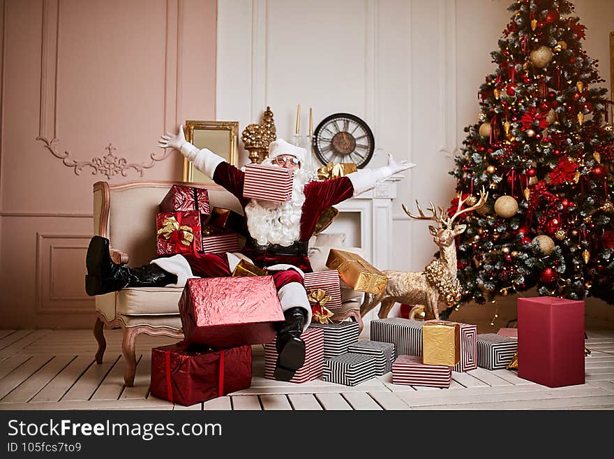 Santa Claus lay down to rest on the sofa with a bunch of gifts near the fireplace and christmas tree . New year and Merry Christmas  , happy holidays concept