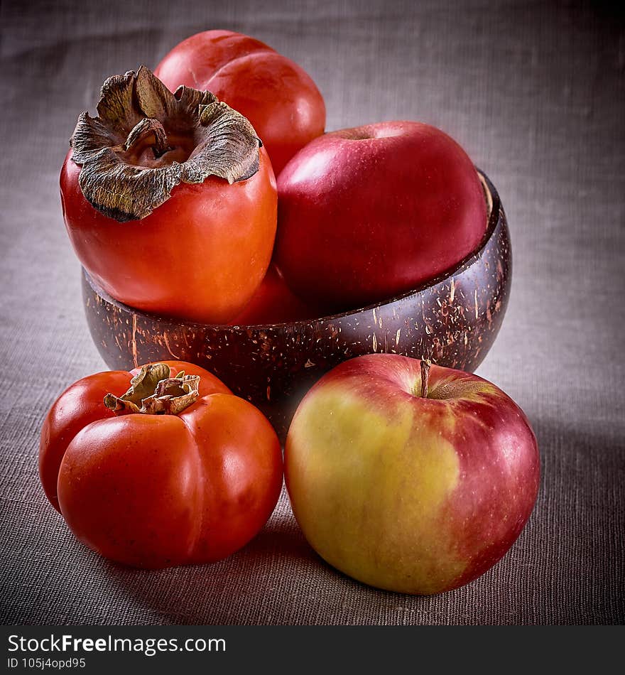 Three orange persimmon fruits on a black plate with Apple slices on a green napkin, top view - the concept of eating seasonal