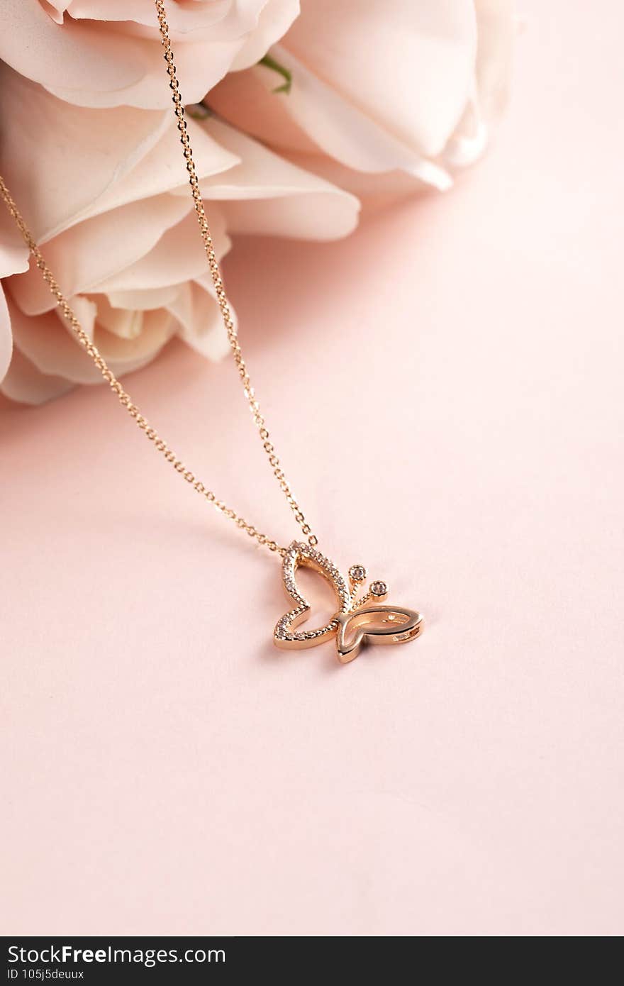 Vertical selective focus closeup of a gold butterfly necklace on a rosy pink background