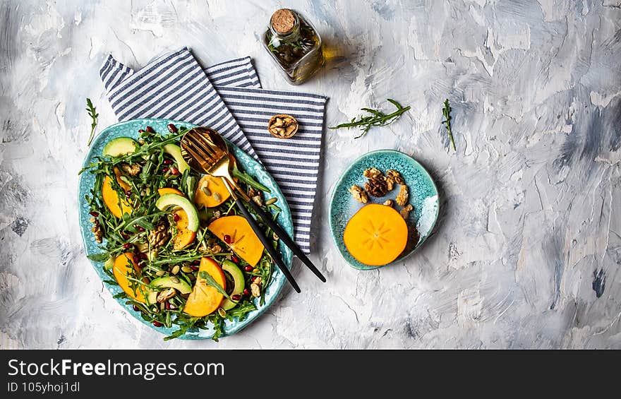 Trendy salad. vegan persimmon salad with arugula, avocado, pumpkin seeds, walnuts, pomegranate. Healthy food, diet lunch concept.