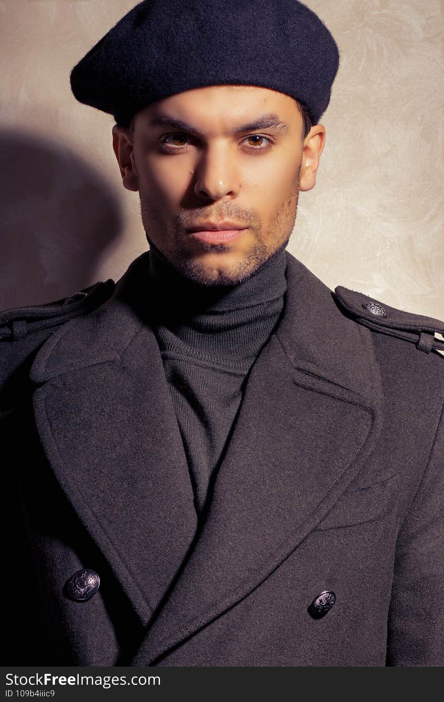 Portrait of a handsome young guy in a beret and a military-style coat.