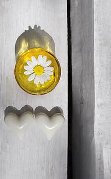 On Light Wooden Background, Yellow Glass Vase With White Chamomile Flower And Two White Ceramic Hearts Stock Images