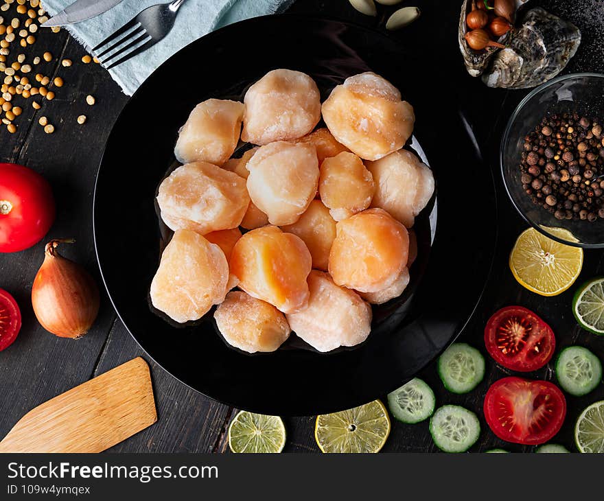 Scallops in a black plate with ingredients. Studio closeup of scallops. Top view. Scallops in a black plate with ingredients. Studio closeup of scallops. Top view.