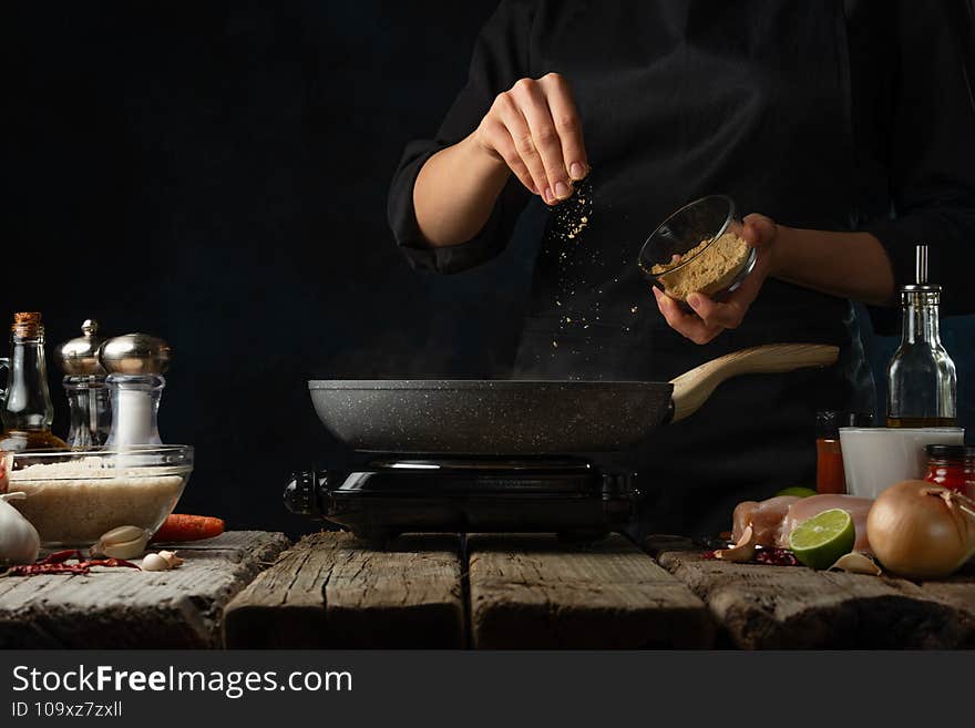 Professional chef pours mustard into pan with frying chicken fillet. Backstage of cooking traditional Indian chicken curry on dark