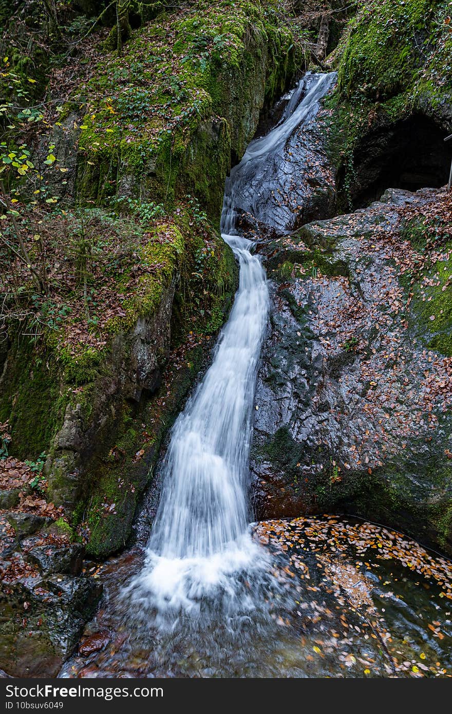 Mystic cascade waterfall in autumn surrounded with green mossy stones and orange leaves