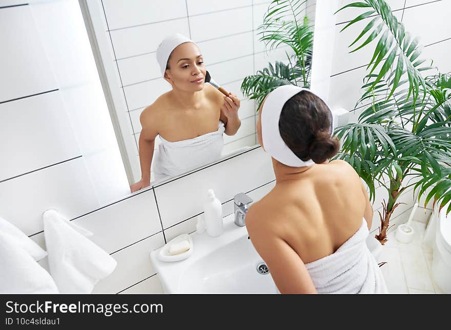 Beautiful young latin american woman applying her blush or face powder before mirror