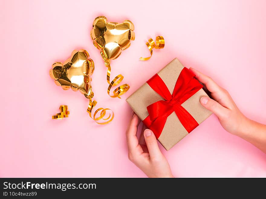 Gold heart shaped balloon and gift box with a red bow on a pink background. Valentine`s day concept. Copy space for text.