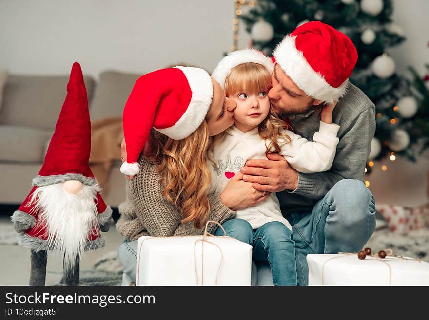 Young family in santa claus hat. Parents kiss their daughter.