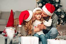 Young Family In Santa Claus Hat. Parents Kiss Their Daughter. Royalty Free Stock Images