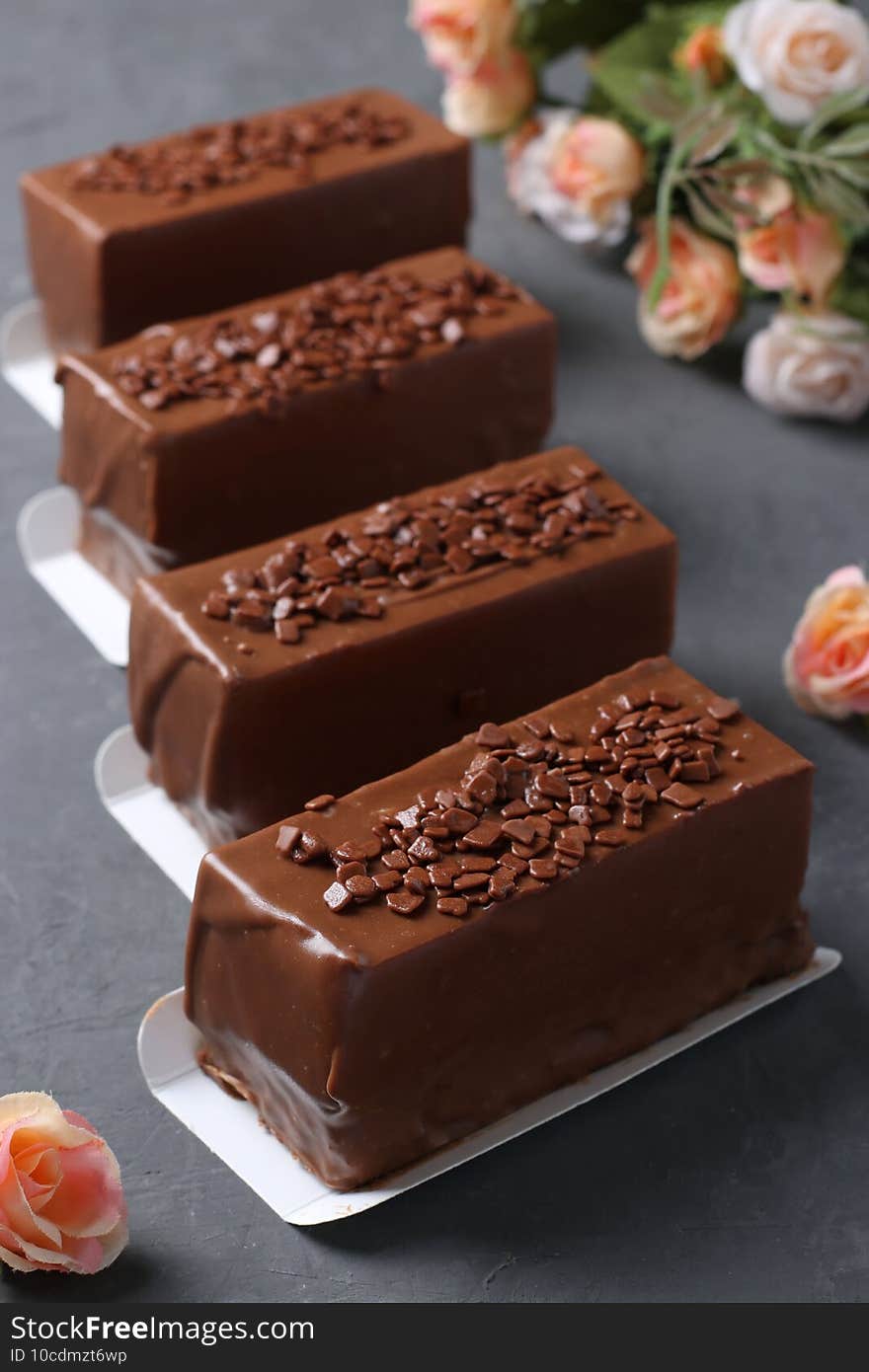 Four mousse desserts covered with chocolate on a dark gray background. Vertical format