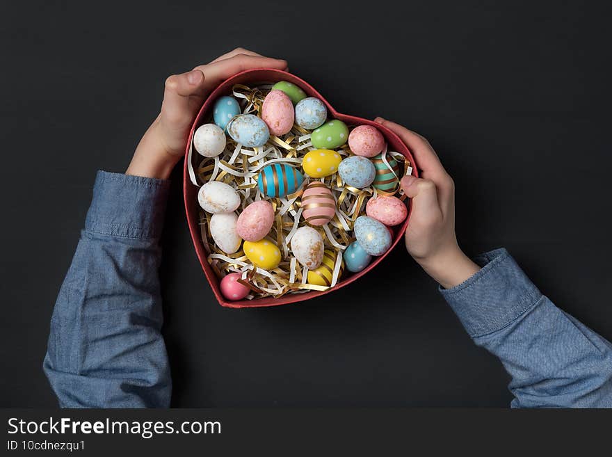 Children holding a Heart shaped box with colorful Easter eggs. Black background. Gift for Easter