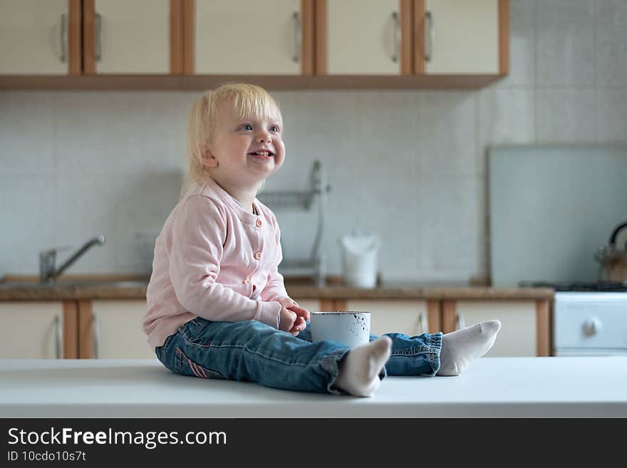 Portrait of smiling blonde child with cup on kitchen table. Breakfast in family