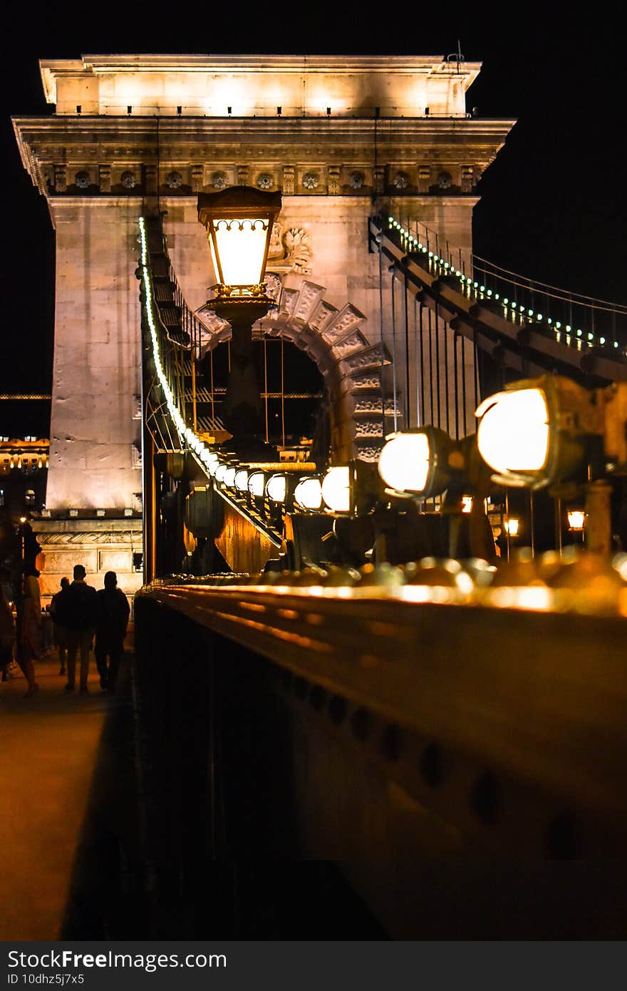 Vertical shot of the Szechenyi Chain Bridge surrounded by lights at night in Budapest, Hungary