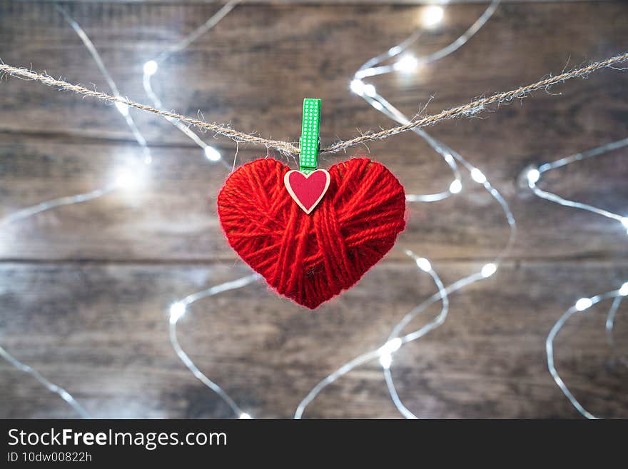 A Red Heart is suspended from a rope against the background of a burning garland.