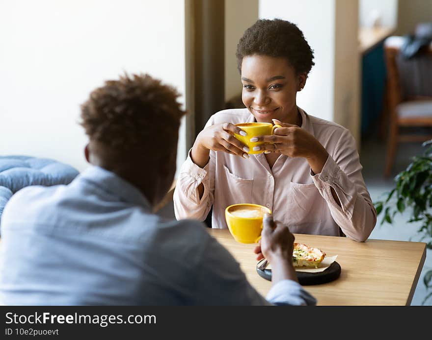 Handsome black man with his girlfriend enjoying aromatic coffee and having friendly conversation at city cafe