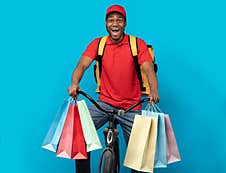 Excited Black Delivery Man Riding Bicycle With Shopping Bags Stock Photos