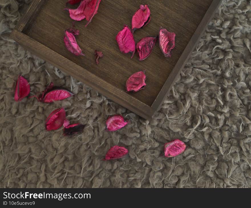 Dry petals of red roses are on a wooden box and soft brown carpet