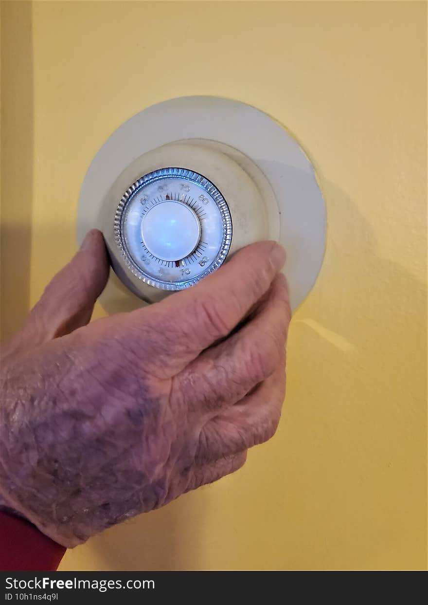 Elderly mans hand turns up wall thermostat