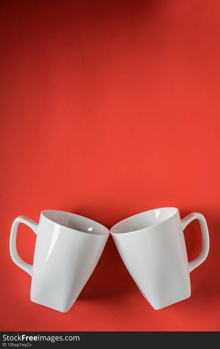 Vertical shot of two white ceramic mugs against a red background