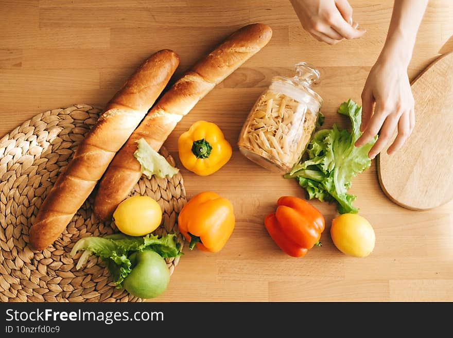 Baguette, pasta and fresh vegetables on a wooden table in the kitchen