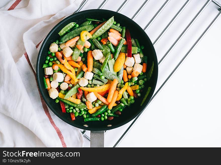 Fresh vegetables mix in a black pan on the white table. Healthy food