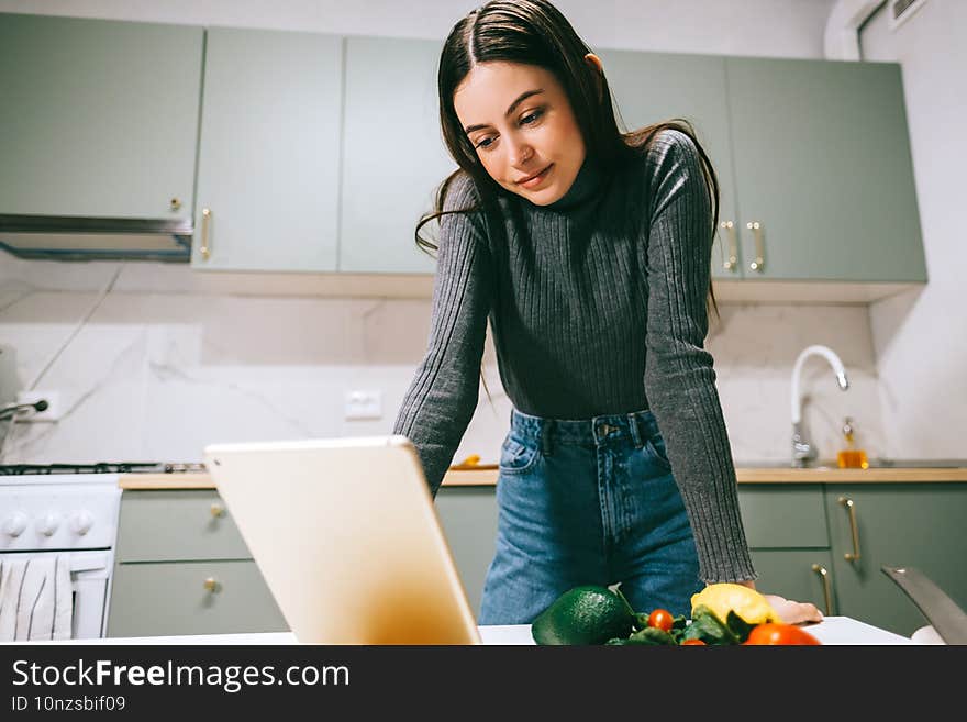 Young caucasian woman use tablet computer in the modern kitchen, preparing salad, read recipe