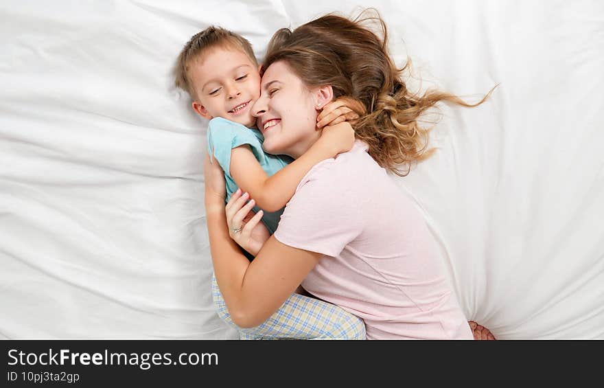 Top view portrait of cute little boy lying with young mother on bed and talking. Concept of parenting and family