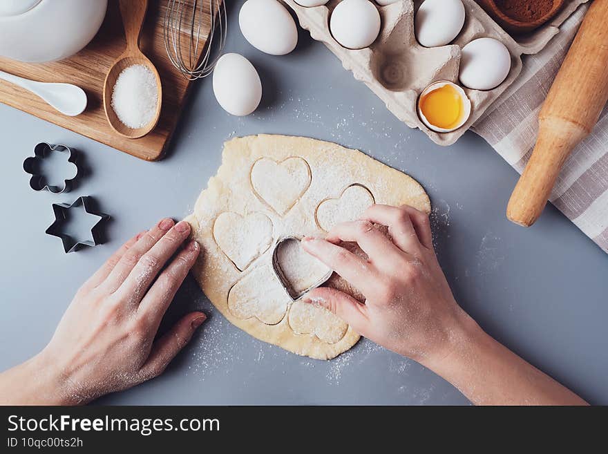 Girl prepares cookies in the shape of a heart, flat lay composition on a gray background. Cookie cutters and dough in women`s