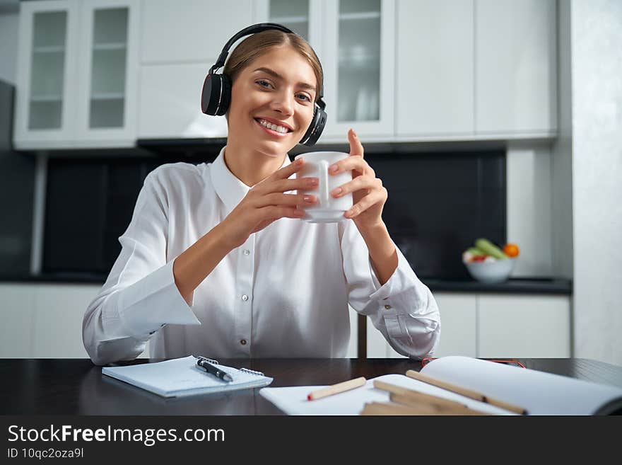 Happy lady in headphones sitting at table and drinking tea