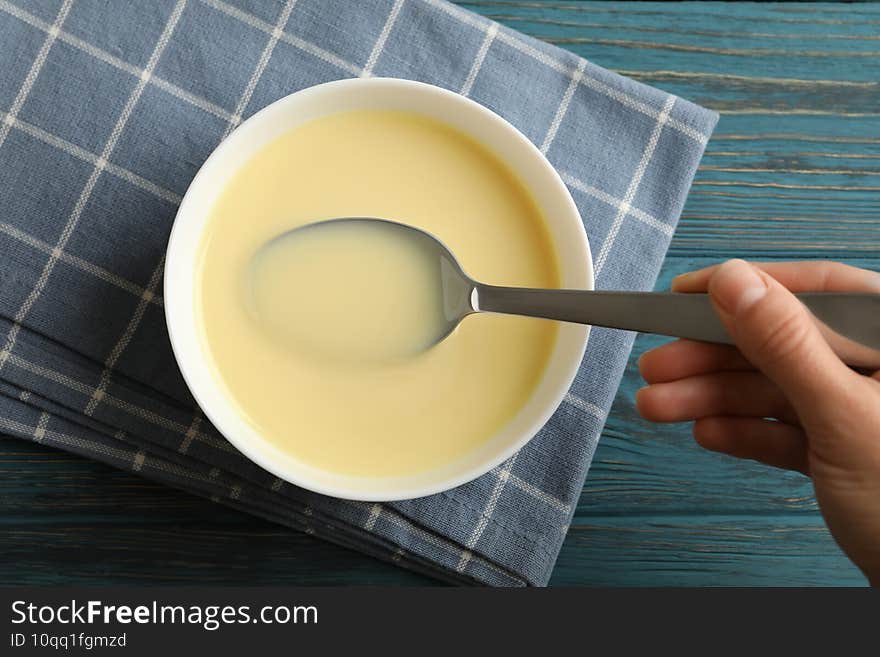 Female hand hold spoon in bowl with condensed milk on towel on wooden background